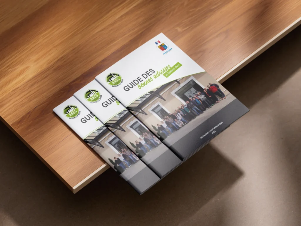 Trois livrets empilés sur une table en bois, dont le titre principal est "GUIDE DES bonnes adresses".