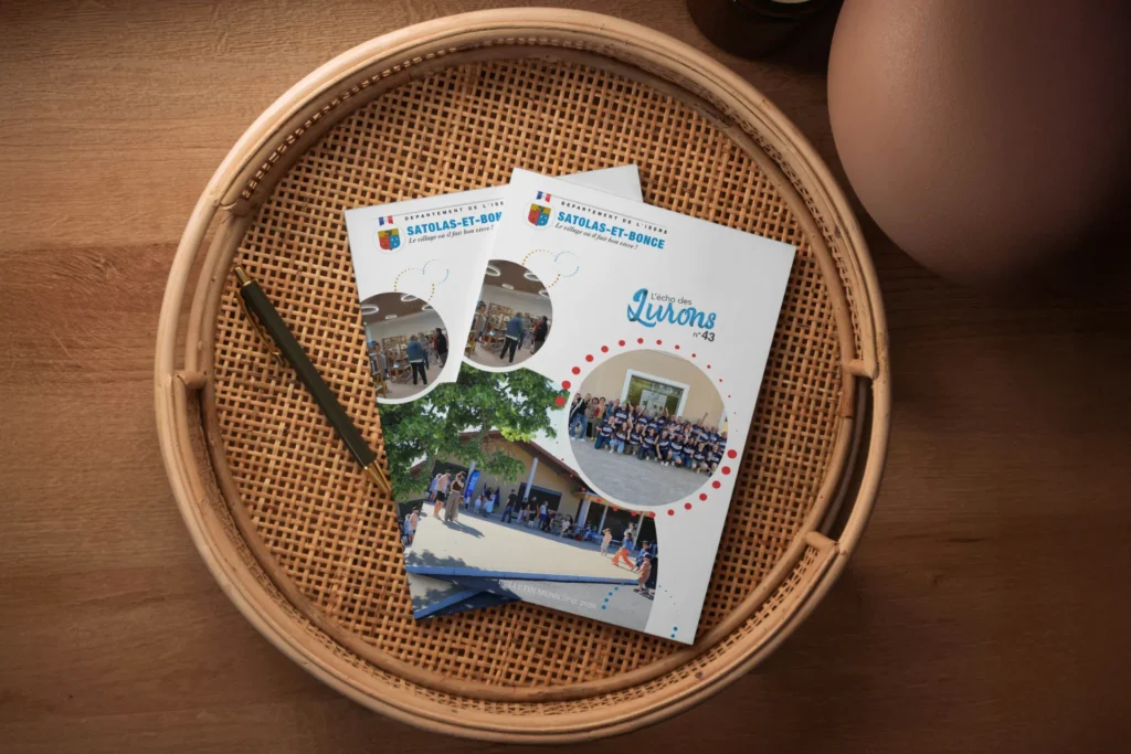 Deux brochures posées sur un plateau en osier. L'une des brochures présente le titre « Les Quérons 43 » avec plusieurs photos circulaires montrant des personnes.