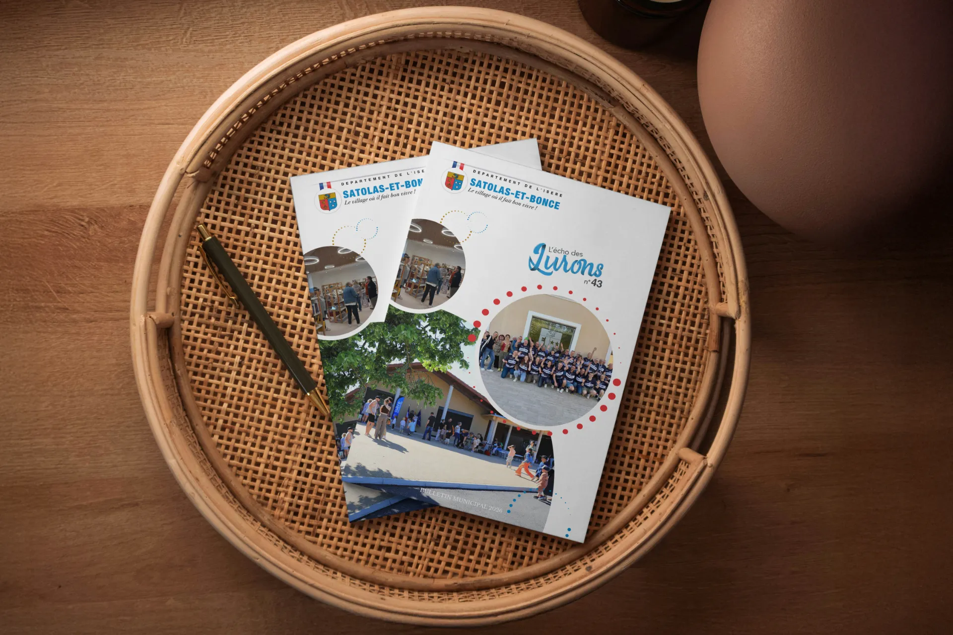 Deux brochures posées sur un plateau en osier. L'une des brochures présente le titre « Les Quérons 43 » avec plusieurs photos circulaires montrant des personnes.