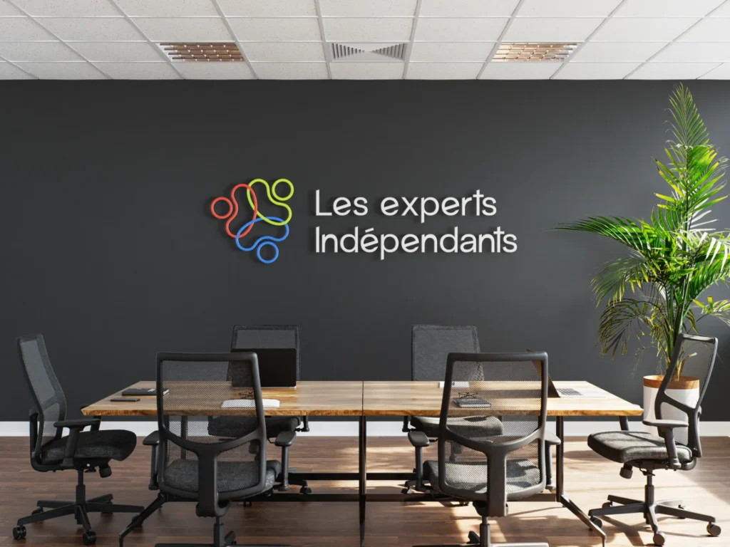Logo coloré "Les experts Indépendants" sur un mur de bureau, avec une table et des chaises.