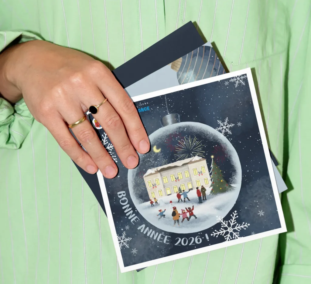 Carte de vœux avec une boule de Noël illuminée contenant une maison enneigée, des feux d'artifice et le message "Bonne Année 2026 !".