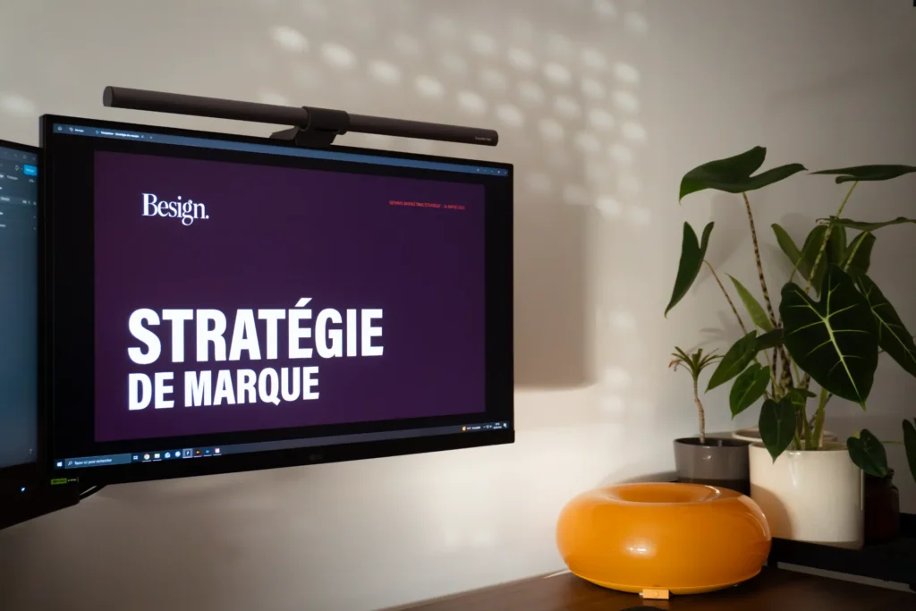 Un écran d'ordinateur affiche "STRATÉGIE DE MARQUE" pour présenter le document de déploiement de stratégie de marque d'une entreprise