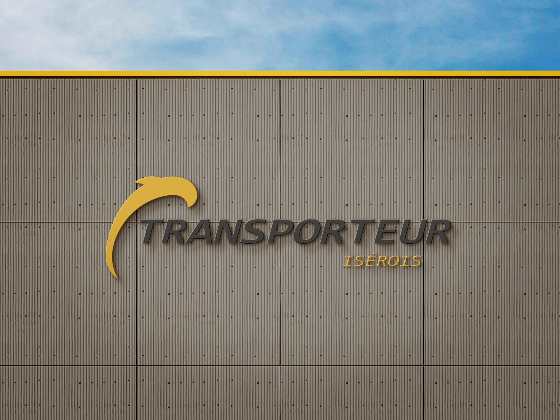 Logo de TRANSPORTEUR ISEROIS sur un mur de bâtiment gris sous un ciel bleu.