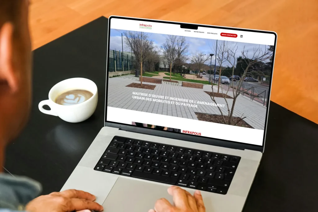Écran d'ordinateur affichant le site Infrapolis, spécialisé en aménagement urbain, avec une photo de paysage et le texte "Maîtrise d'œuvre et ingénierie de l'aménagement urbain des mobilités et du paysage".