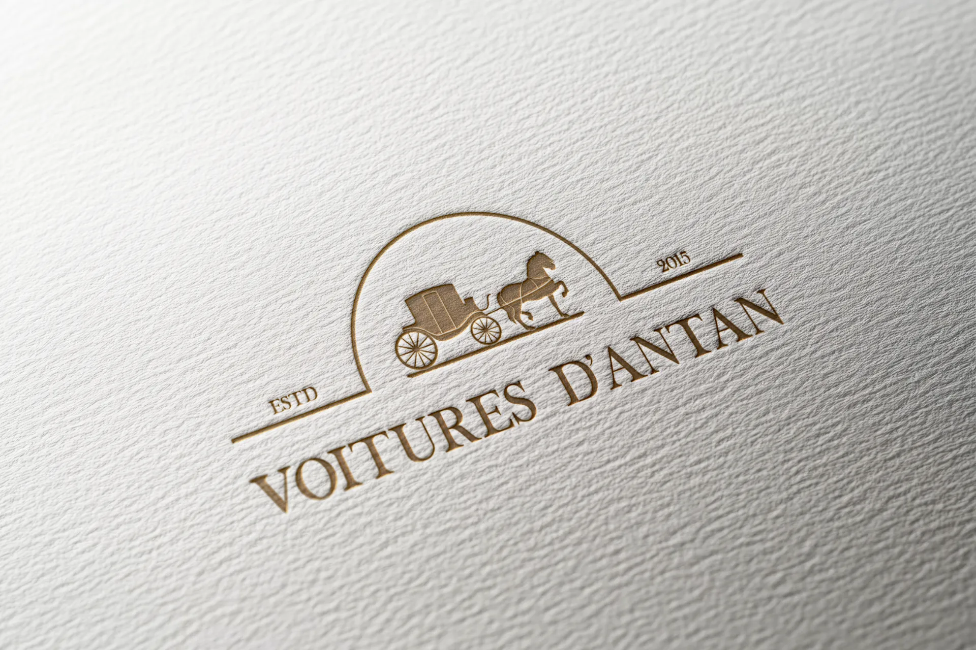 Logo doré 'Voitures D'Antan' avec une calèche tirée par un cheval, datant de 2015.