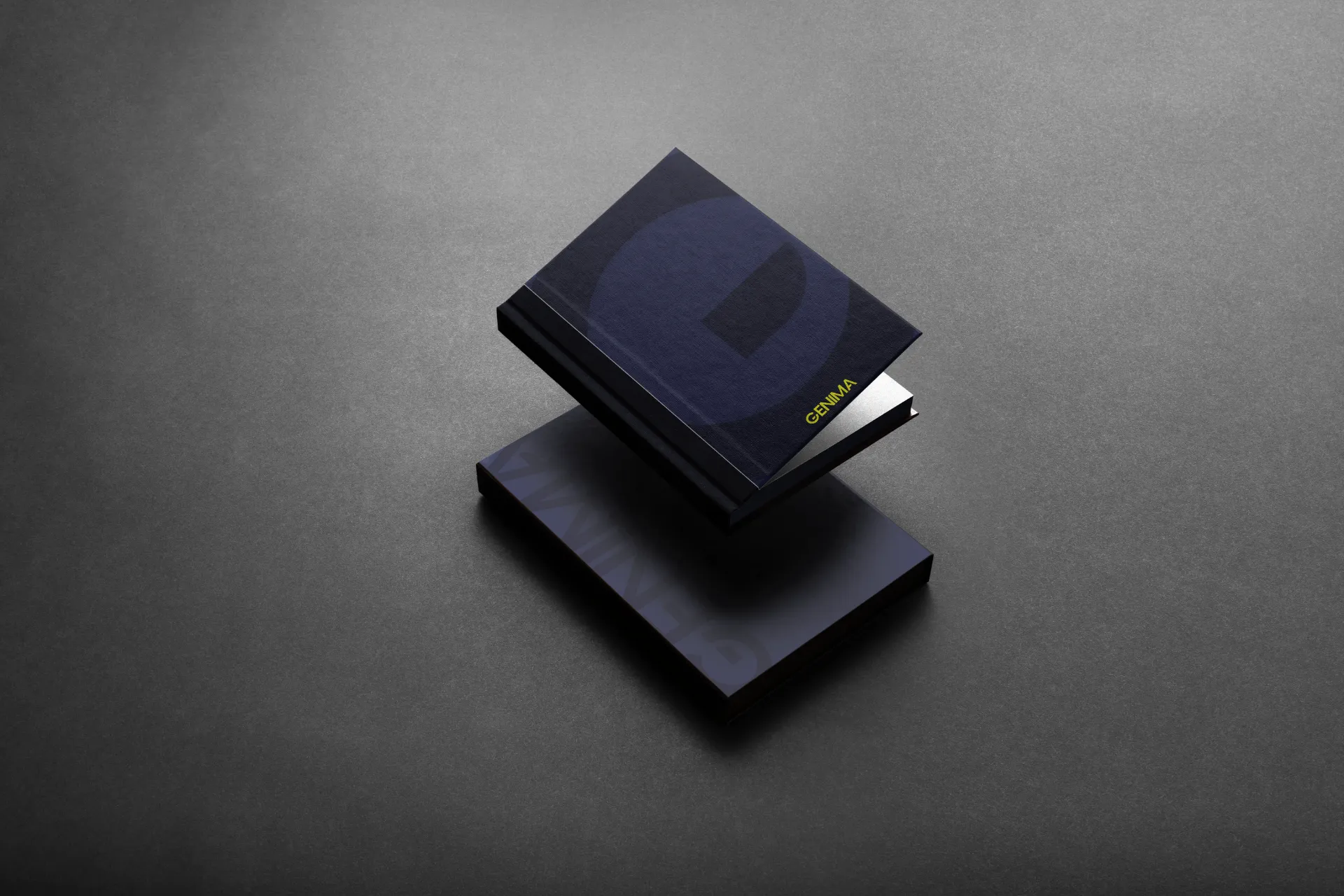 Livre relié bleu nuit avec le logo de GENIMA en lettres dorées, posé sur un autre livre sombre
